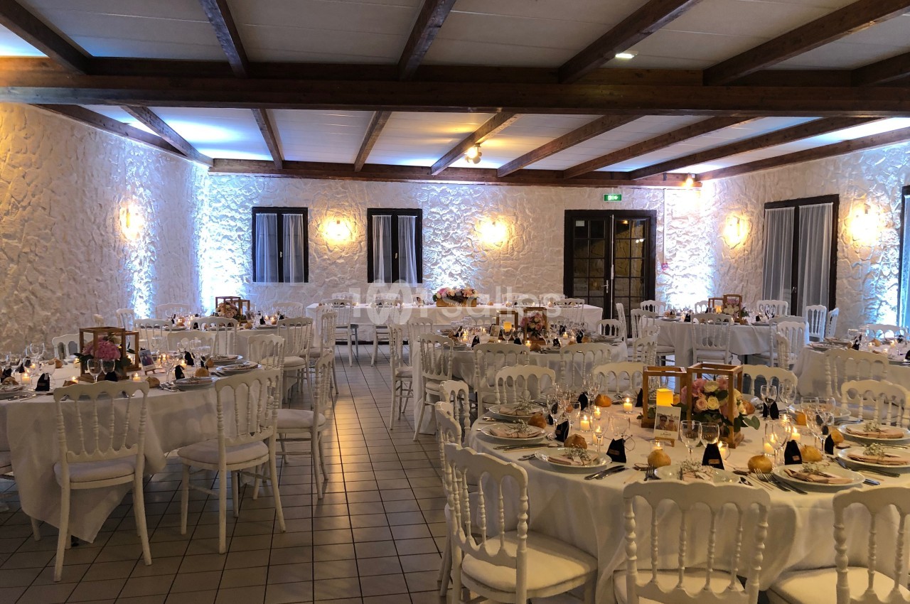 Salle de réception décorée avec des tables rondes dressées, nappes blanches et éclairage tamisé.