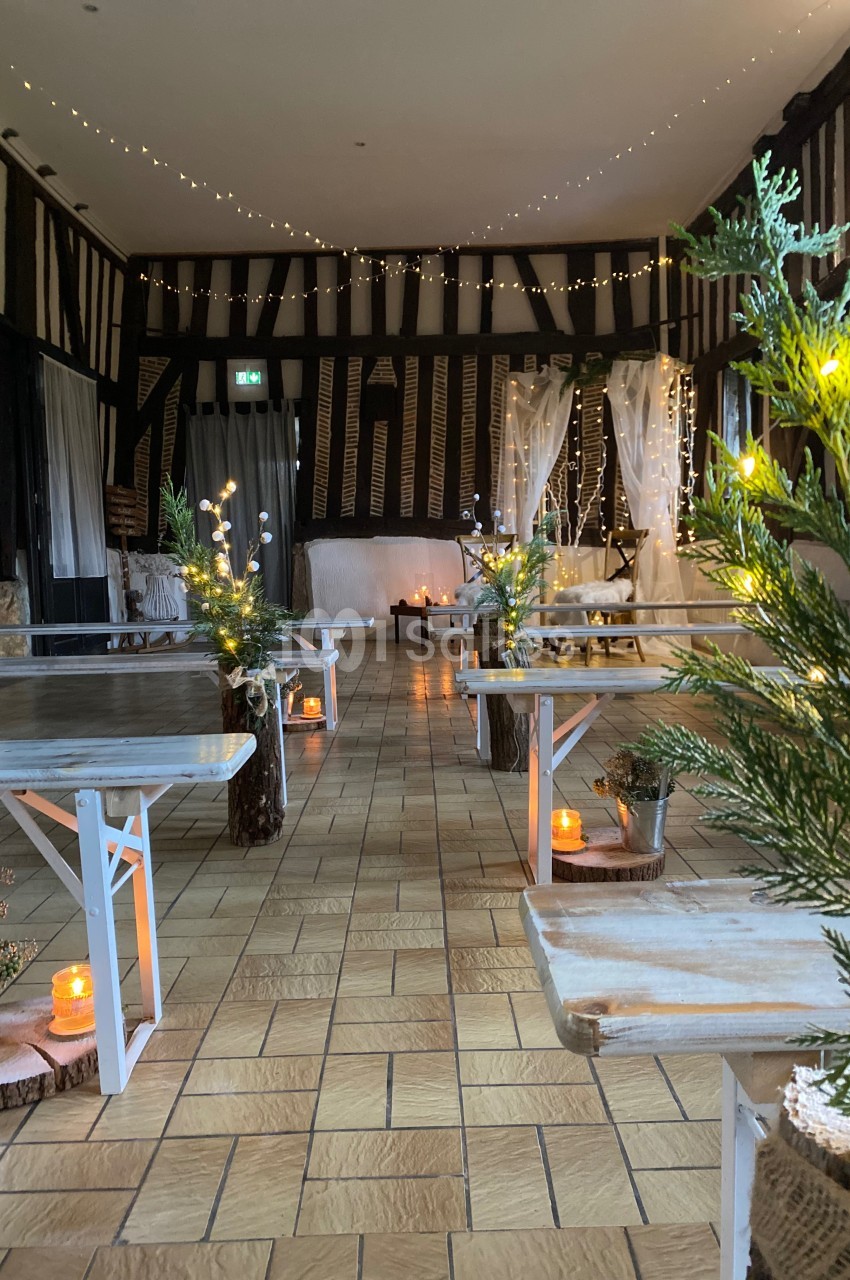 Salle décorée pour un événement, avec bancs en bois, bougies, guirlandes lumineuses et plantes sur un sol carrelé.