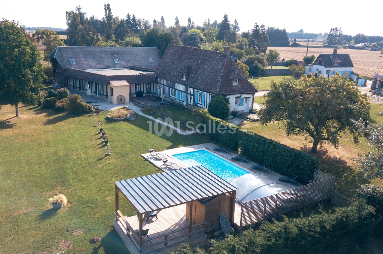Vue aérienne d'une maison traditionnelle avec piscine, terrasse couverte et grand jardin arboré en campagne.
