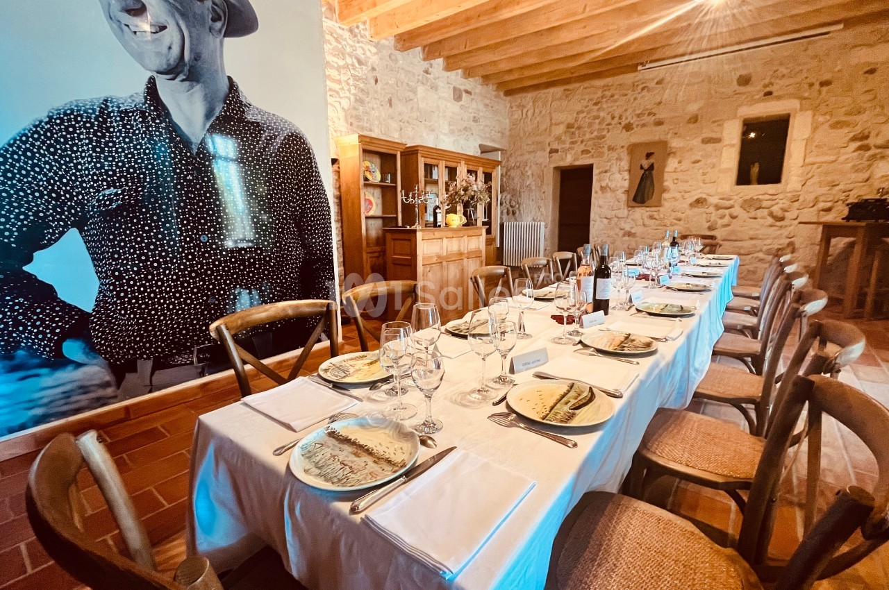Table dressée pour un repas dans une salle en pierre avec poutres apparentes et une grande photo en noir et blanc au mur.