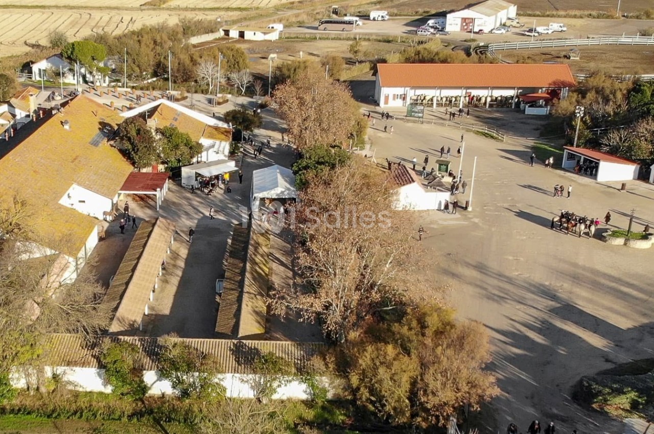 Vue aérienne d'un domaine rural avec bâtiments traditionnels, espaces ouverts et quelques arbres en automne.