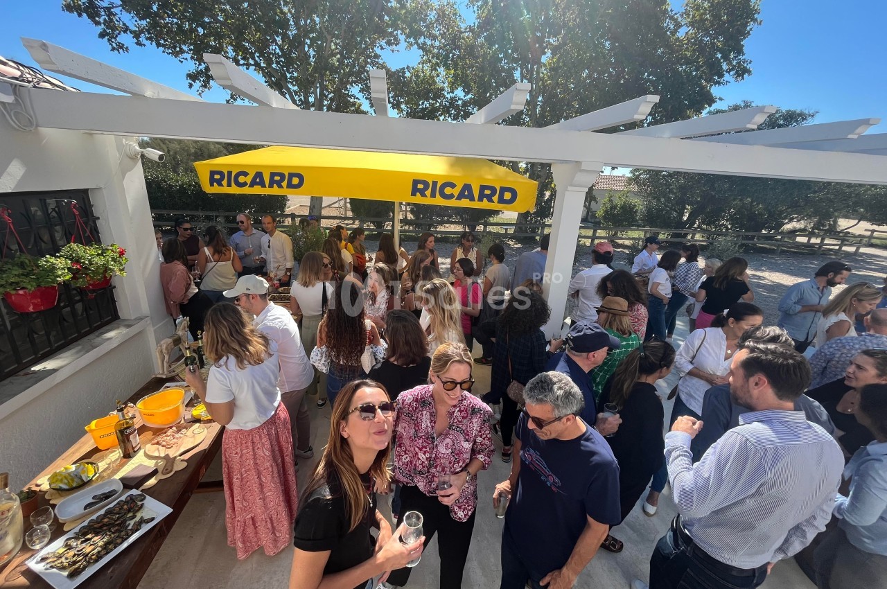 Groupe de personnes rassemblées en extérieur sous un auvent jaune, discutant et partageant un moment convivial.