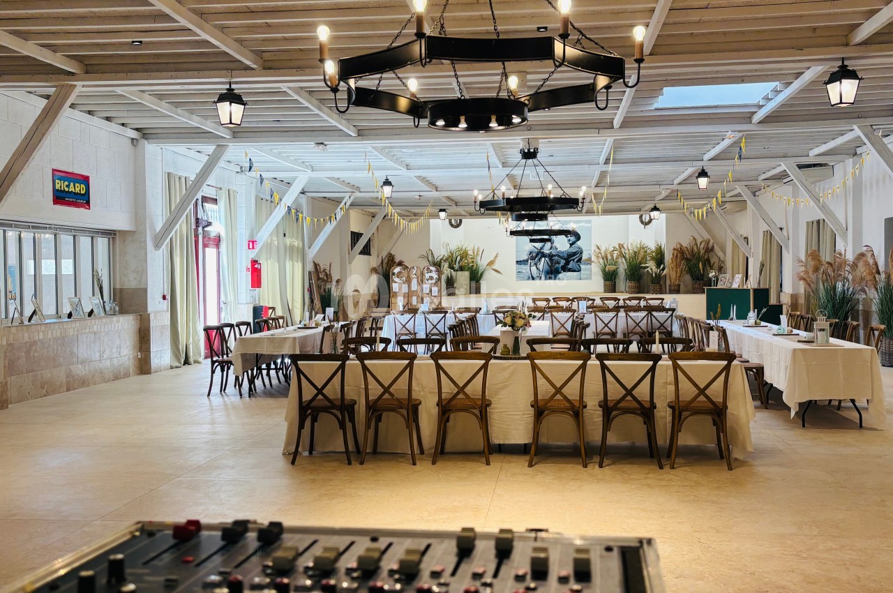 Salle de réception lumineuse avec tables dressées, décor rustique et console de mixage au premier plan.