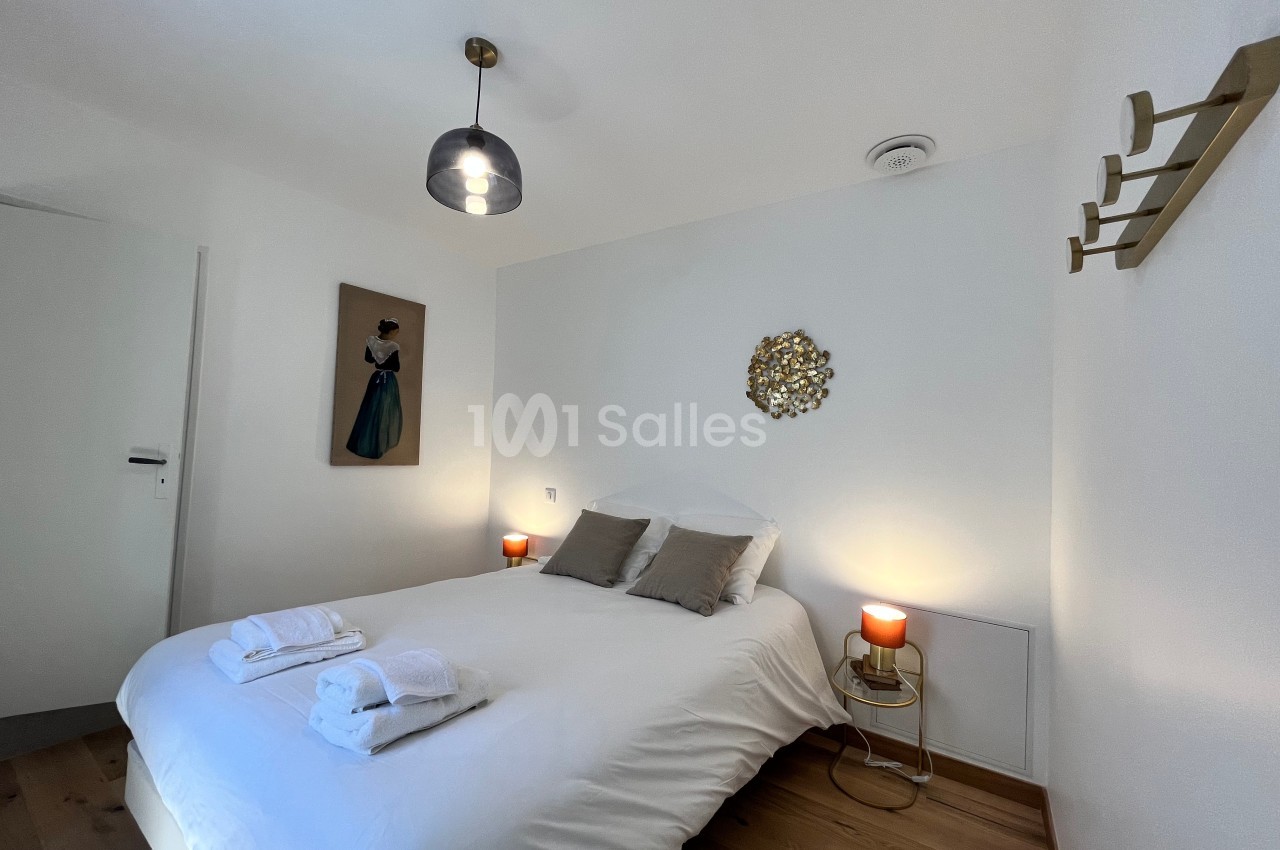 Chambre lumineuse avec lit double, décor sobre, deux lampes de chevet et des serviettes pliées sur le lit.