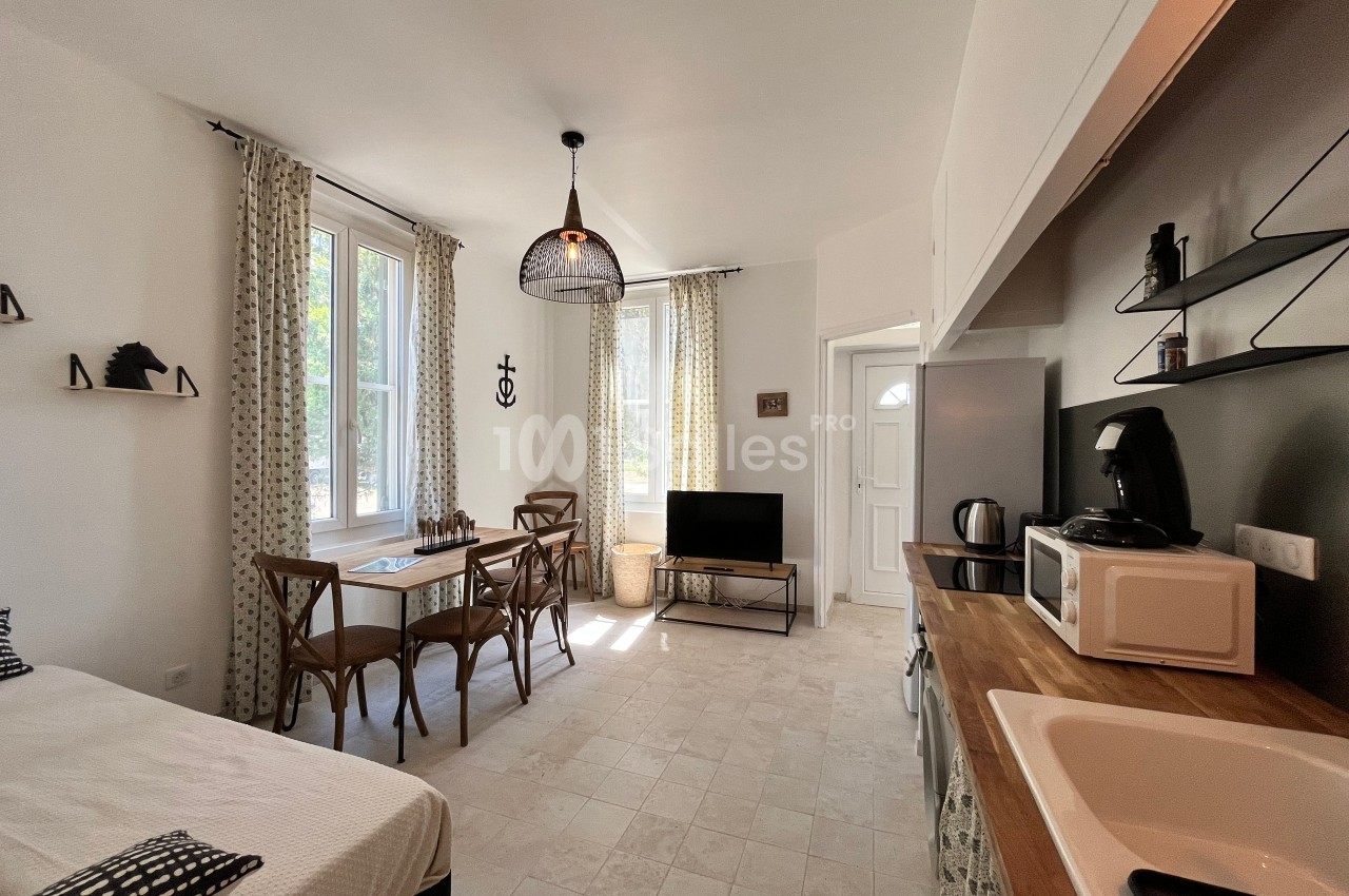 Studio lumineux avec coin salon, table à manger, cuisine équipée et grandes fenêtres donnant sur l'extérieur.