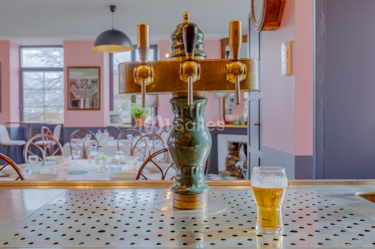 Pompe à bière en laiton sur un comptoir, avec un verre de bière rempli, dans un intérieur de café coloré.