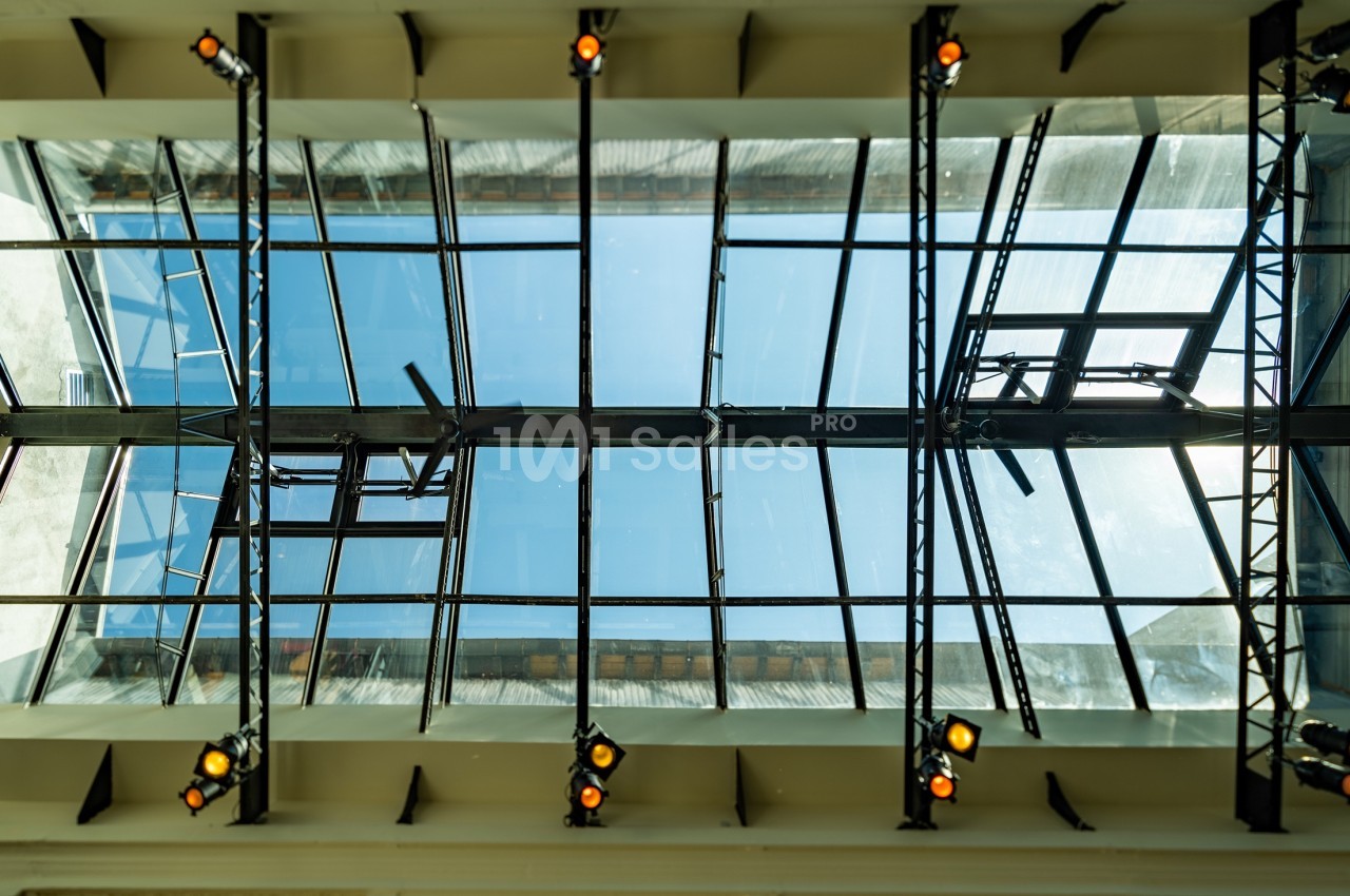 Vue en contre-plongée d'une verrière moderne avec des structures métalliques et des projecteurs fixés.