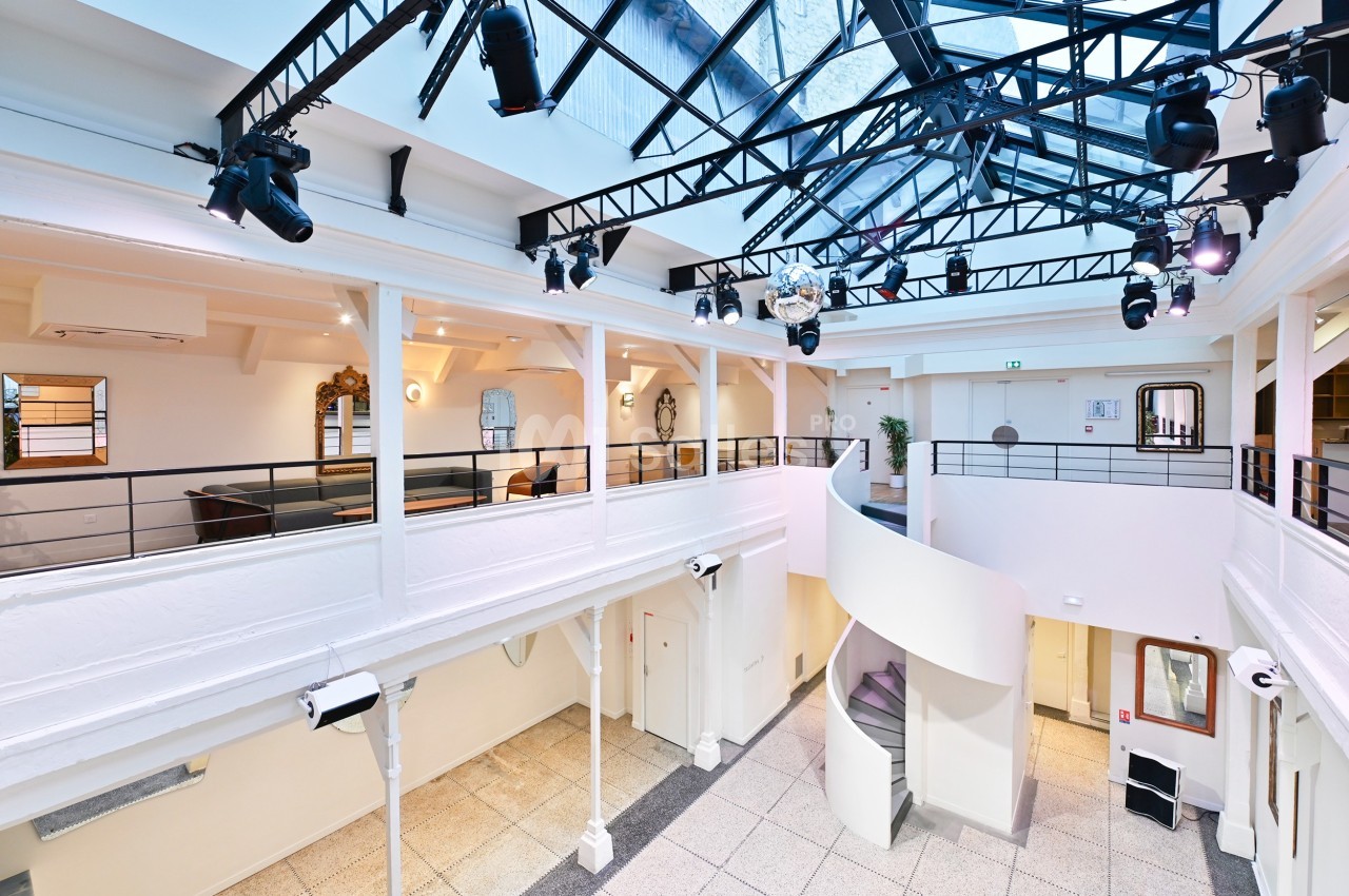 Intérieur d'un espace lumineux avec mezzanine, verrière, escalier en colimaçon et éclairage suspendu.