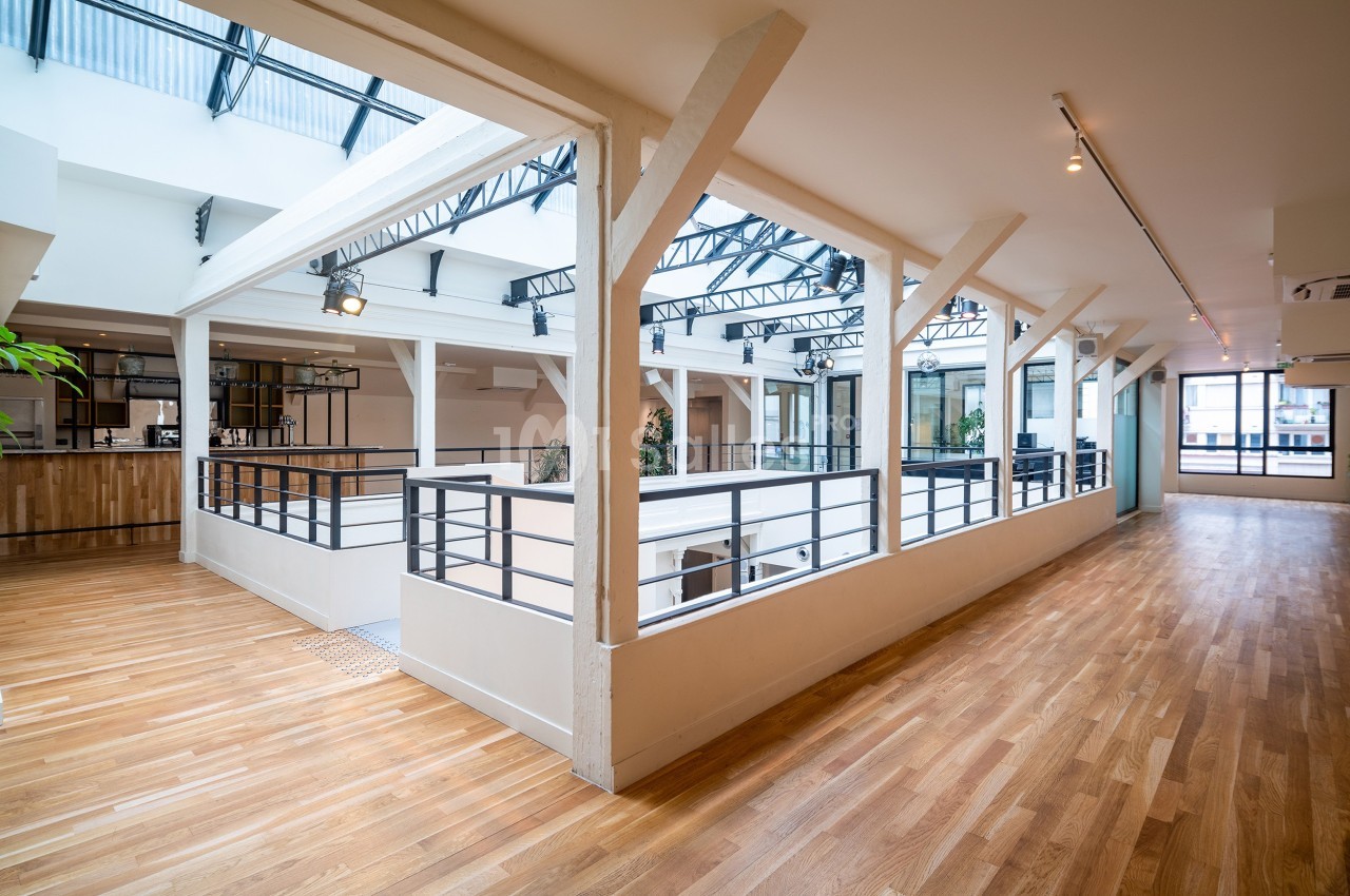 Espace intérieur lumineux avec parquet, verrière et balustrades blanches, donnant sur un étage inférieur.
