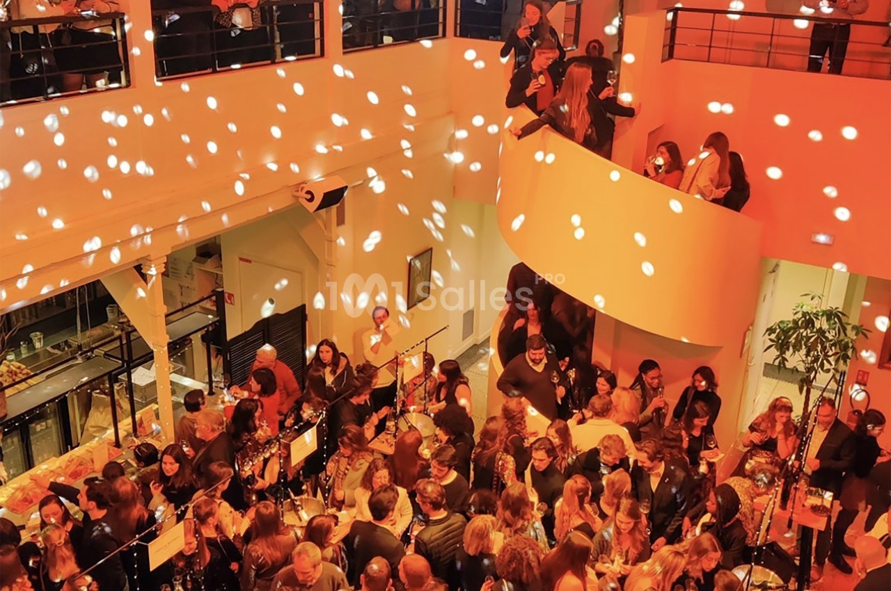Salle animée avec de nombreuses personnes réunies lors d'un événement, éclairée par des lumières tamisées et des spots.