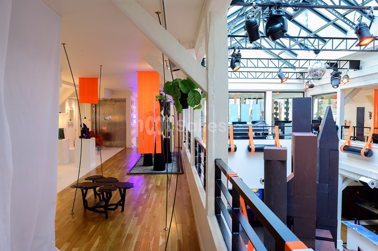 Intérieur lumineux avec mezzanine, verrière, mobilier moderne et éléments décoratifs orange et noirs.