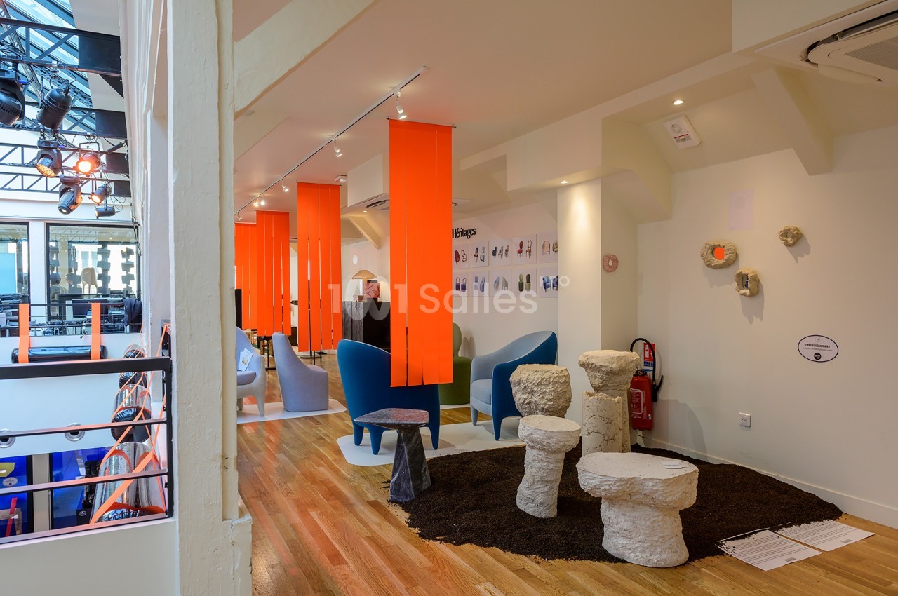 Espace intérieur lumineux avec mobilier design, chaises colorées, tabourets sculptés et panneaux orange suspendus.