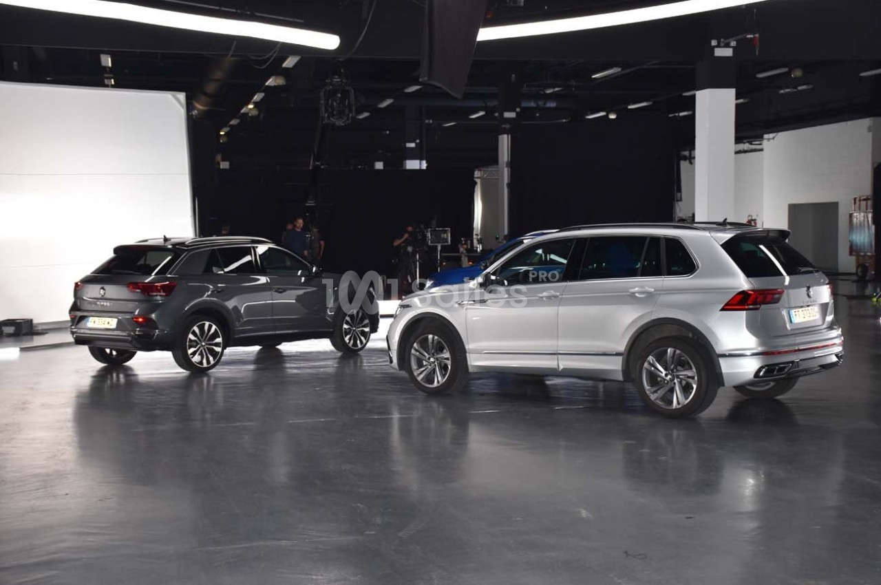 Deux SUV stationnés dans un studio lumineux avec un sol en béton et un fond noir.