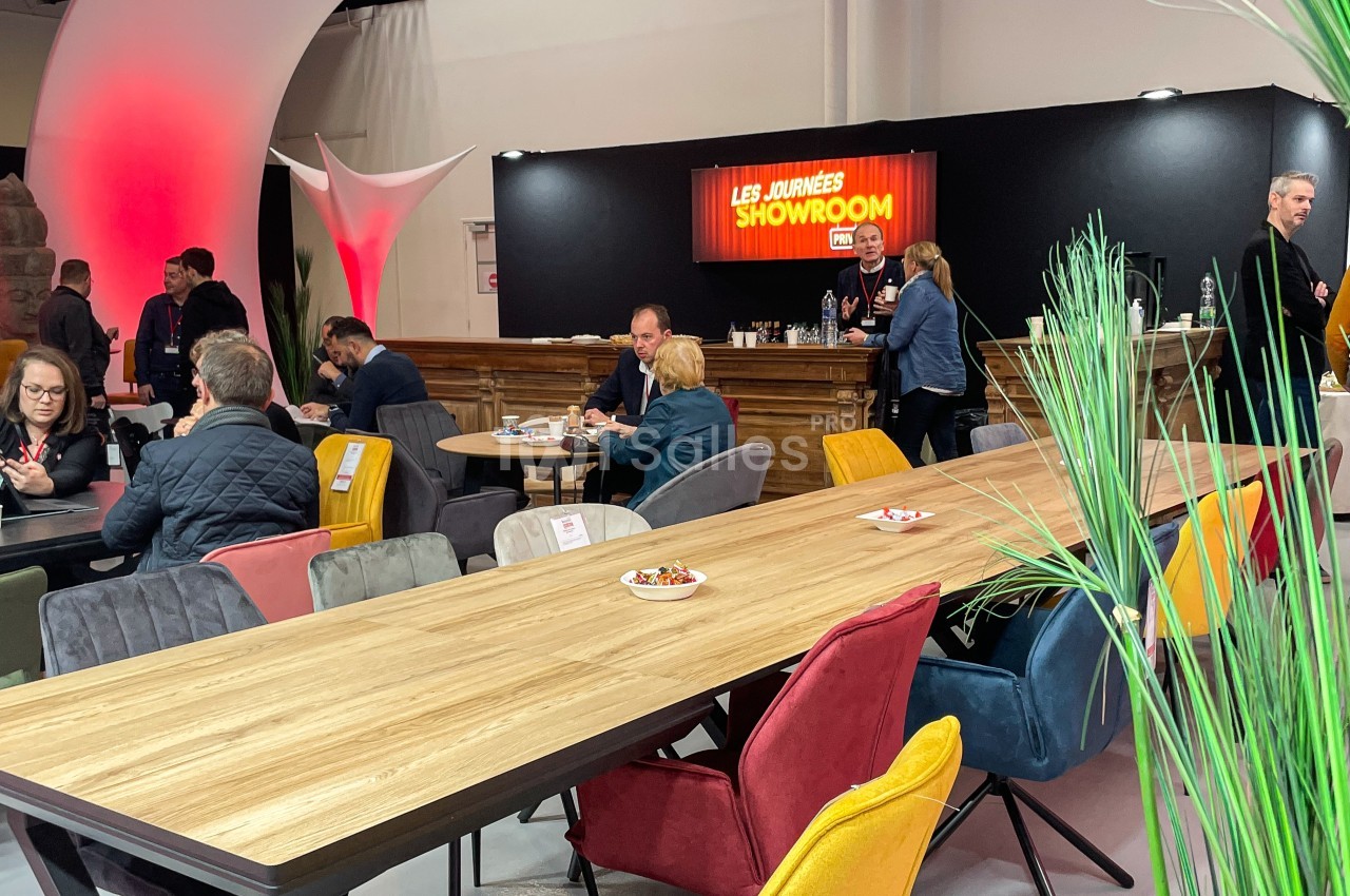 Des personnes discutent et travaillent autour de tables en bois dans un espace showroom avec un éclairage chaleureux.