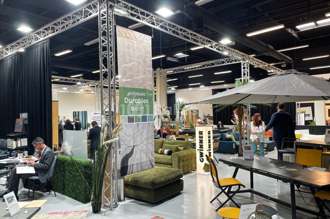 Salon d'exposition intérieur avec stands de meubles, décoration et visiteurs circulant entre les espaces aménagés.