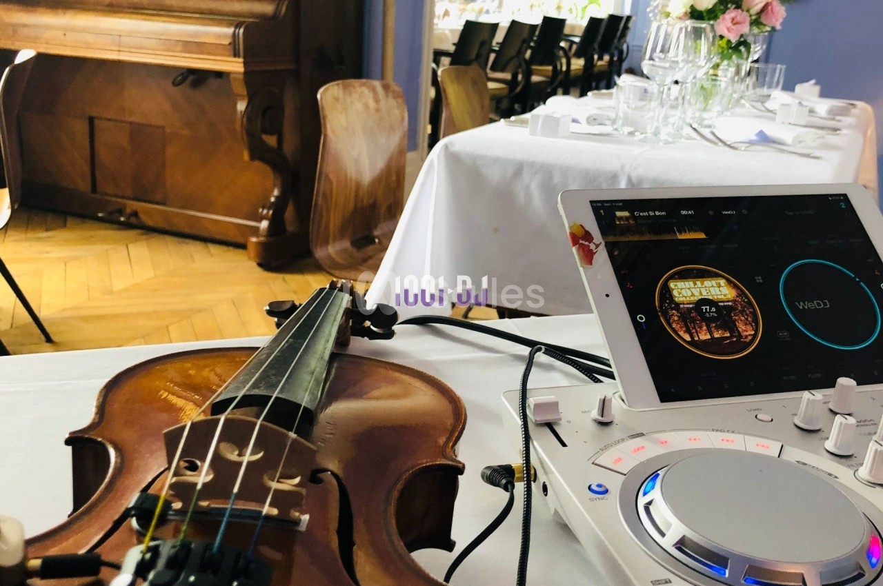Un violon posé sur une table près d'un contrôleur DJ, dans une salle avec des tables dressées.