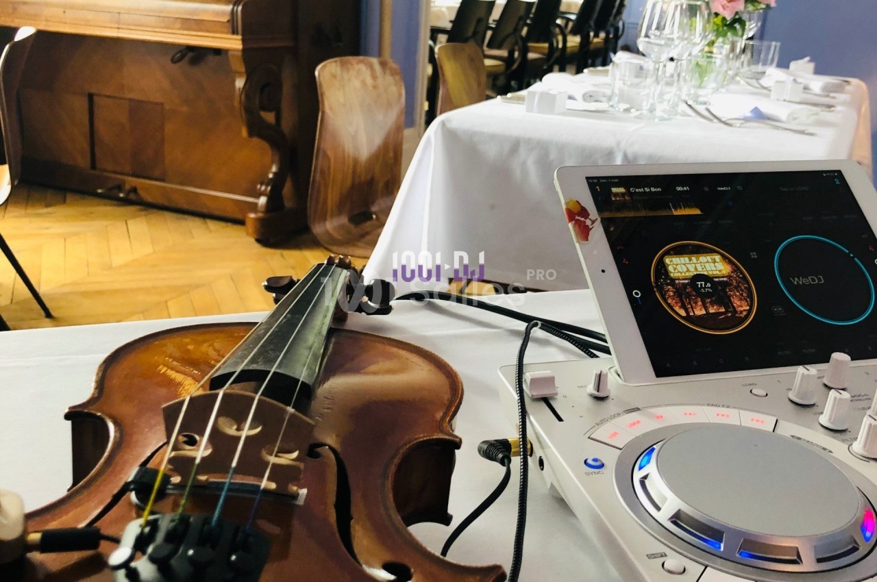 Un violon posé sur une table près d'une console DJ et d'une tablette dans une salle de réception.