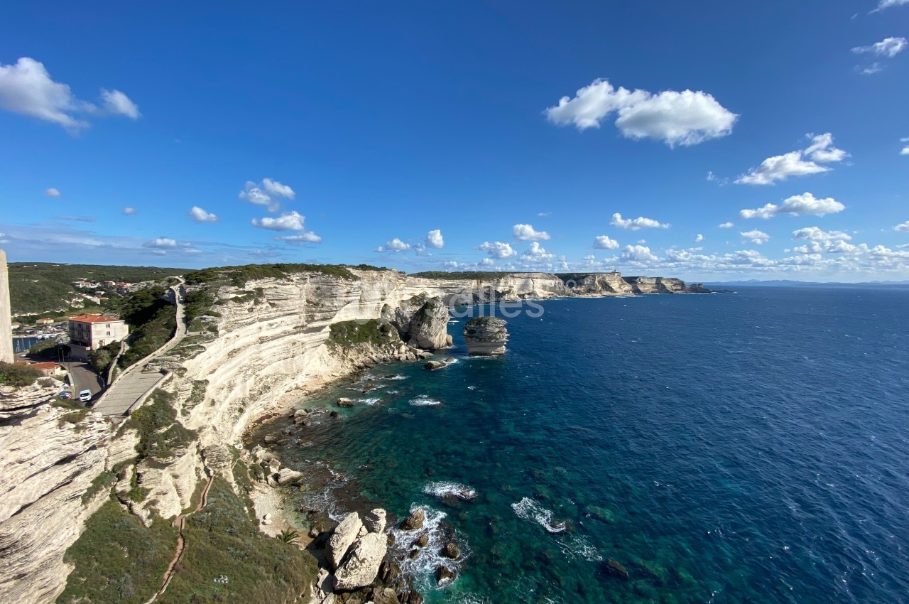 Falaises blanches surplombant une mer bleue avec un ciel dégagé et quelques nuages, vue côtière panoramique.