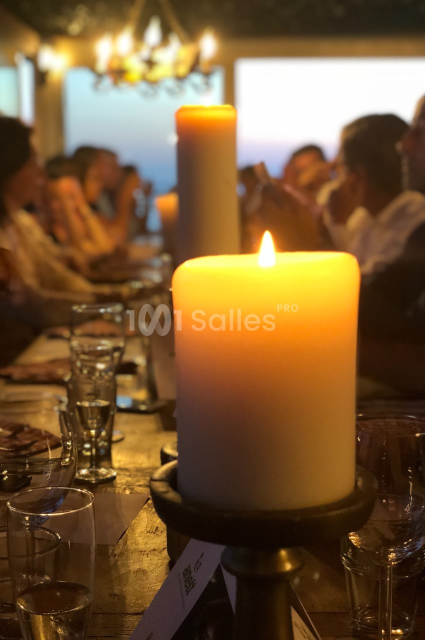 Bougie allumée au centre d'une table entourée de convives flous dans une ambiance chaleureuse et tamisée.