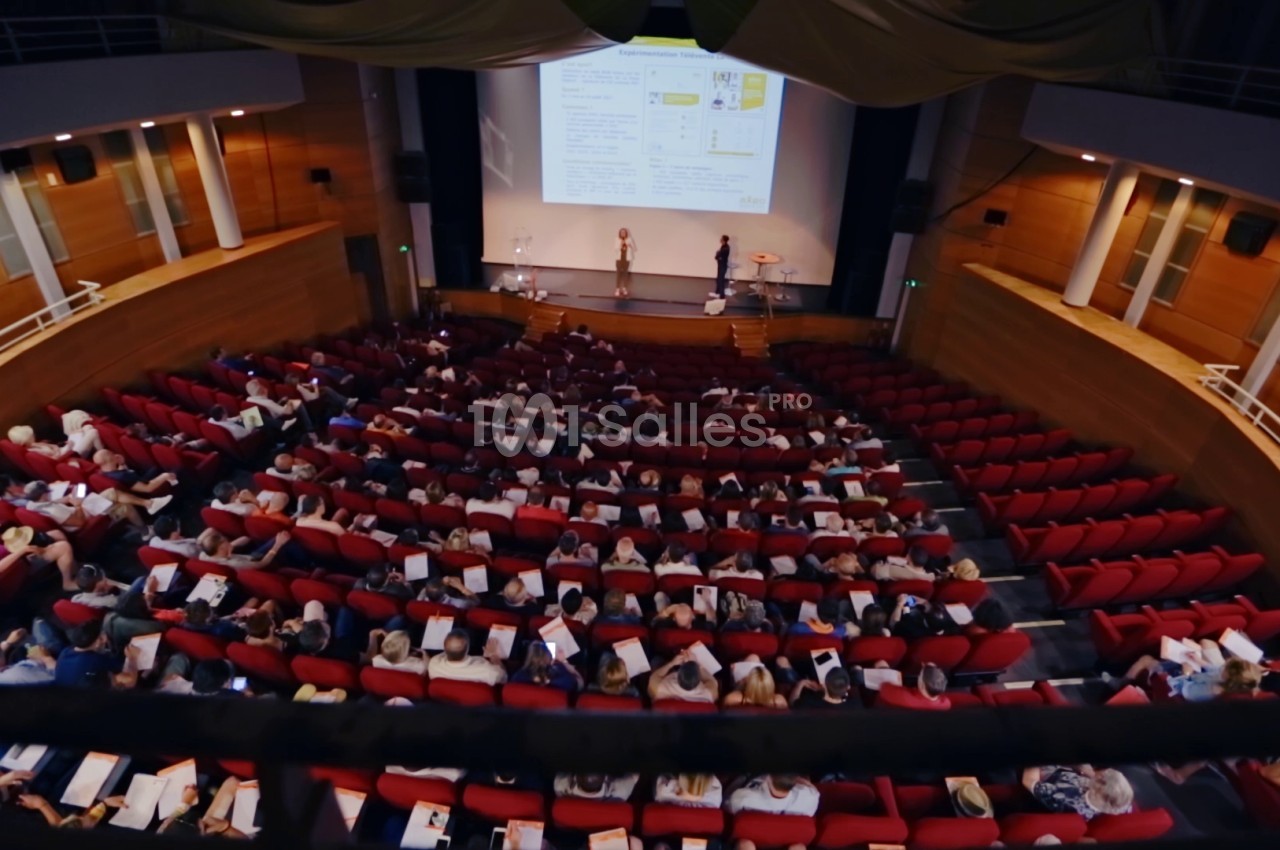 Vue d'une salle de conférence avec des participants assis et un écran projetant une présentation.
