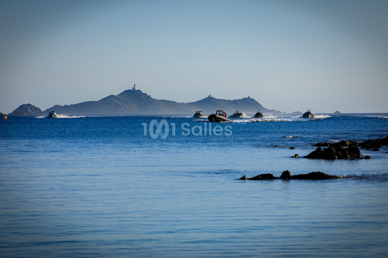 Vue sur une mer calme avec plusieurs bateaux rapides naviguant près d'une île rocheuse à l'horizon.