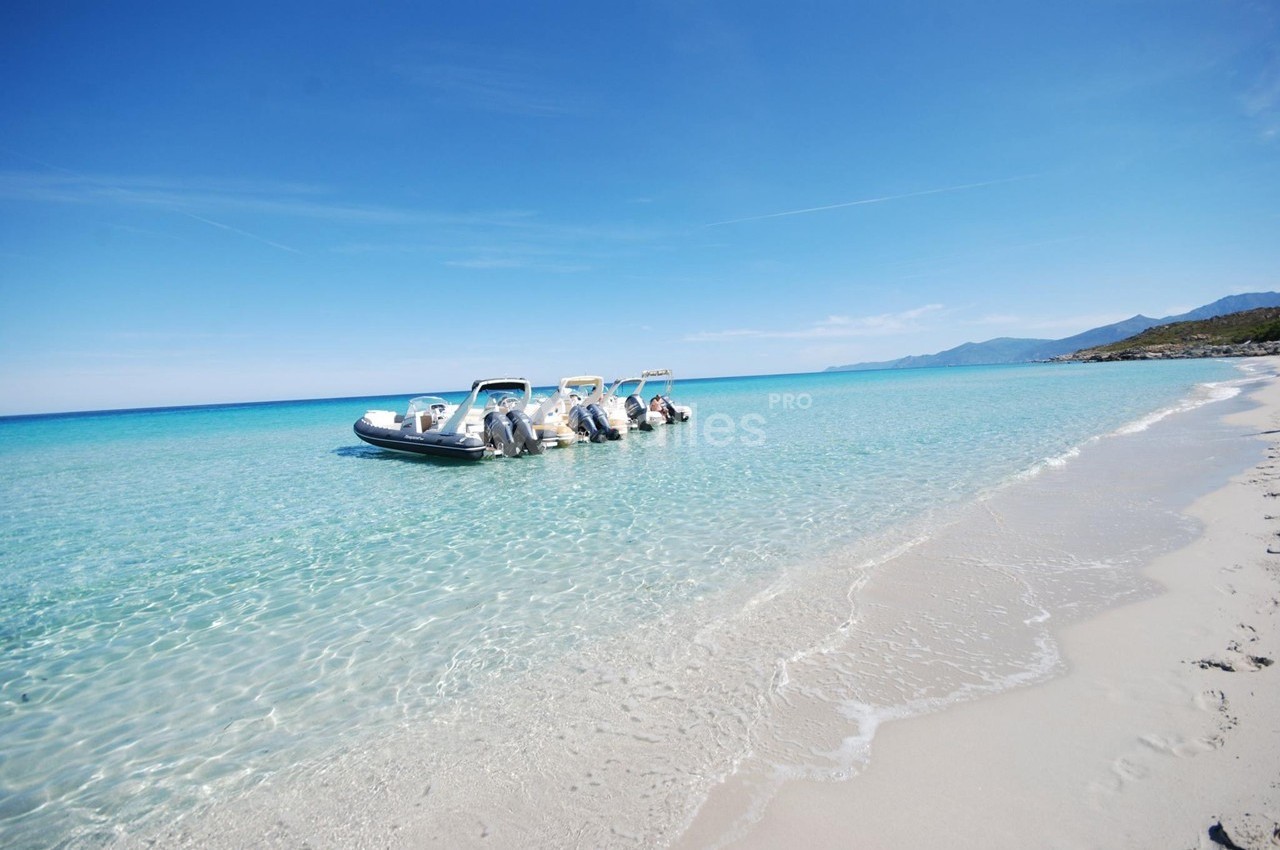Quatre bateaux pneumatiques amarrés sur une plage de sable blanc, dans une eau turquoise sous un ciel dégagé.