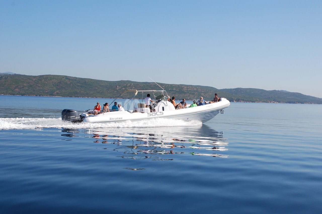 Un bateau pneumatique avec des passagers navigue sur une mer calme, avec des collines en arrière-plan.