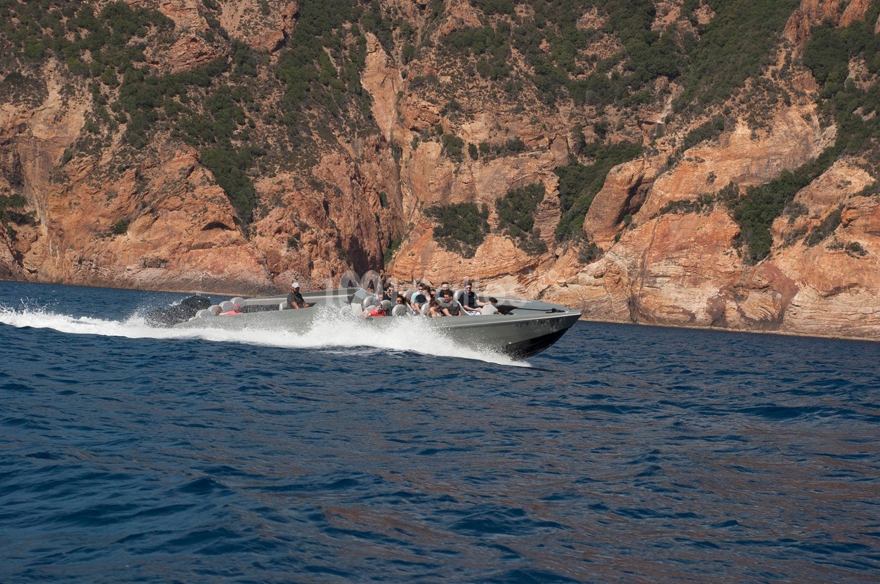 Un bateau rapide transportant des passagers navigue sur une mer bleue, avec des falaises rocheuses en arrière-plan.
