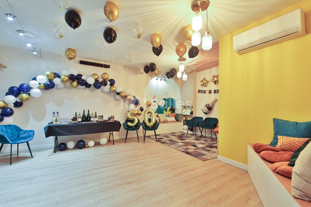 Salle décorée pour un 50e anniversaire avec ballons dorés et noirs, table dressée et coin salon coloré.