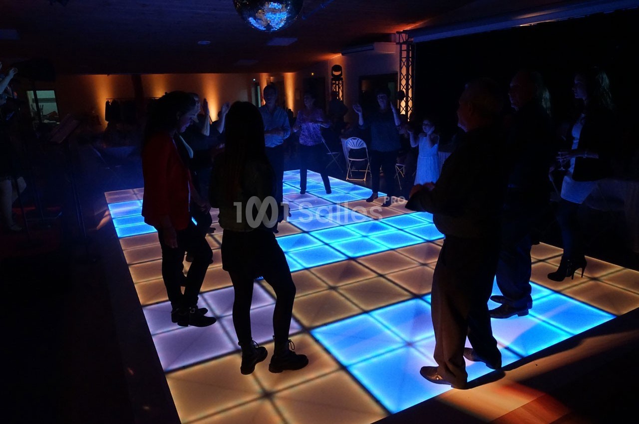 Personnes dansant sur une piste lumineuse à carreaux bleus dans une salle faiblement éclairée.