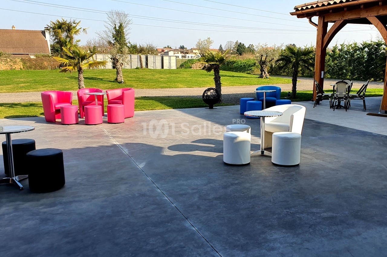Mobilier coloré disposé sur une terrasse en béton, avec des palmiers et un espace vert en arrière-plan.