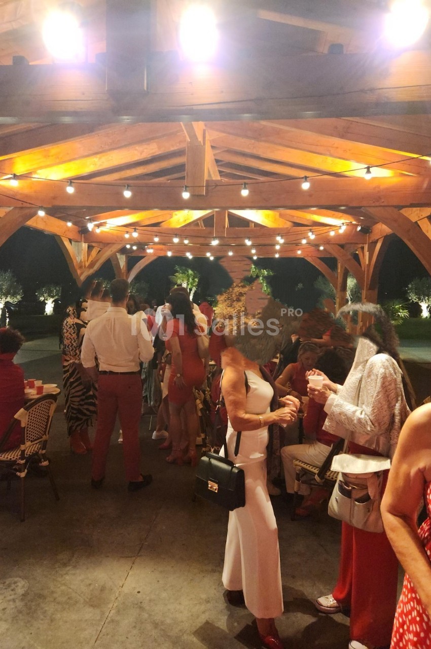 Groupe de personnes discutant sous une pergola en bois éclairée, lors d'un événement en soirée.