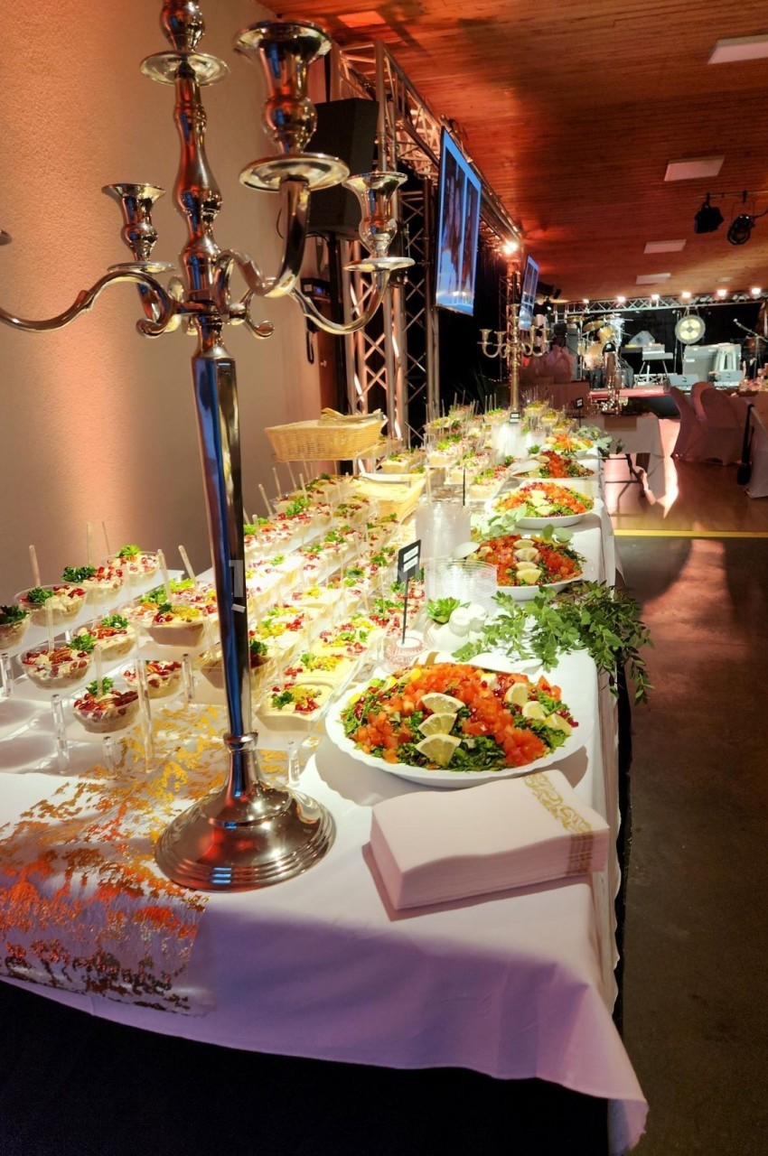 Buffet élégant avec plats variés, salades, verrines et décorations raffinées sous un éclairage chaleureux.