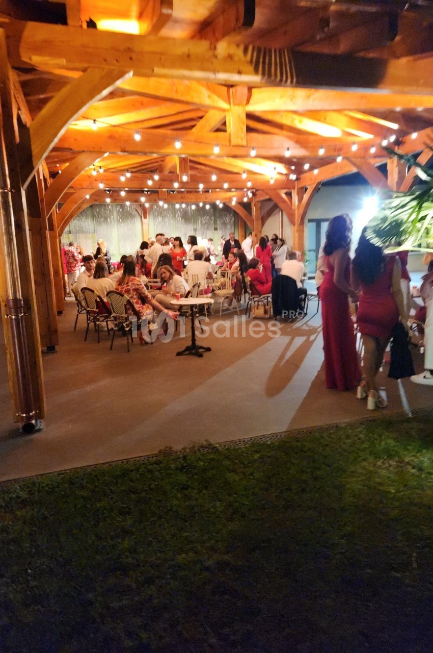 Groupe de personnes assises et debout sous une pergola en bois éclairée par des guirlandes lumineuses.