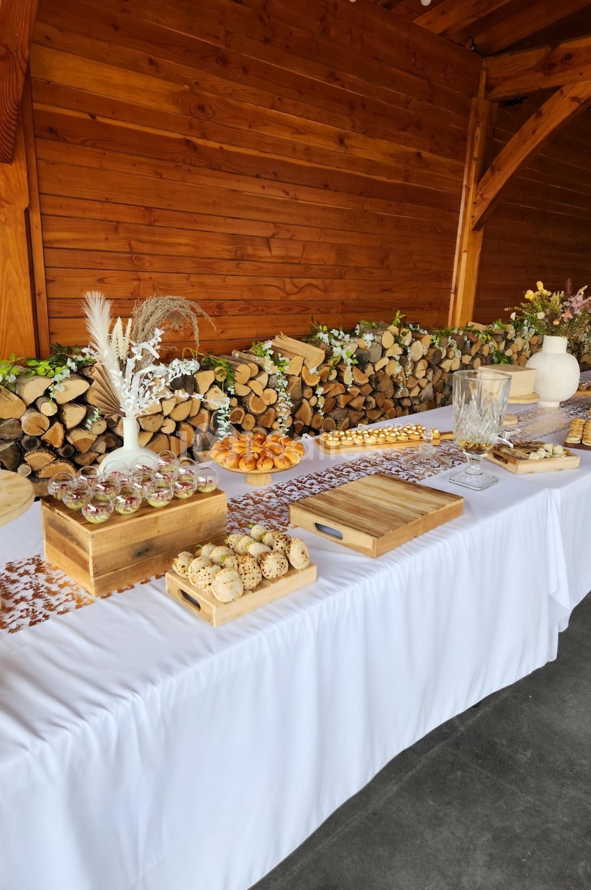 Table dressée avec nappes blanches, assortiments de desserts et décor rustique en bois et feuillages.