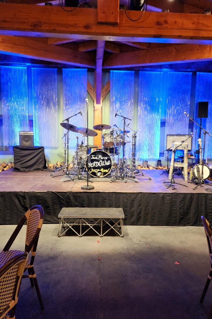 Scène de concert vide avec batterie, percussions et amplificateur, éclairée par des lumières bleues.