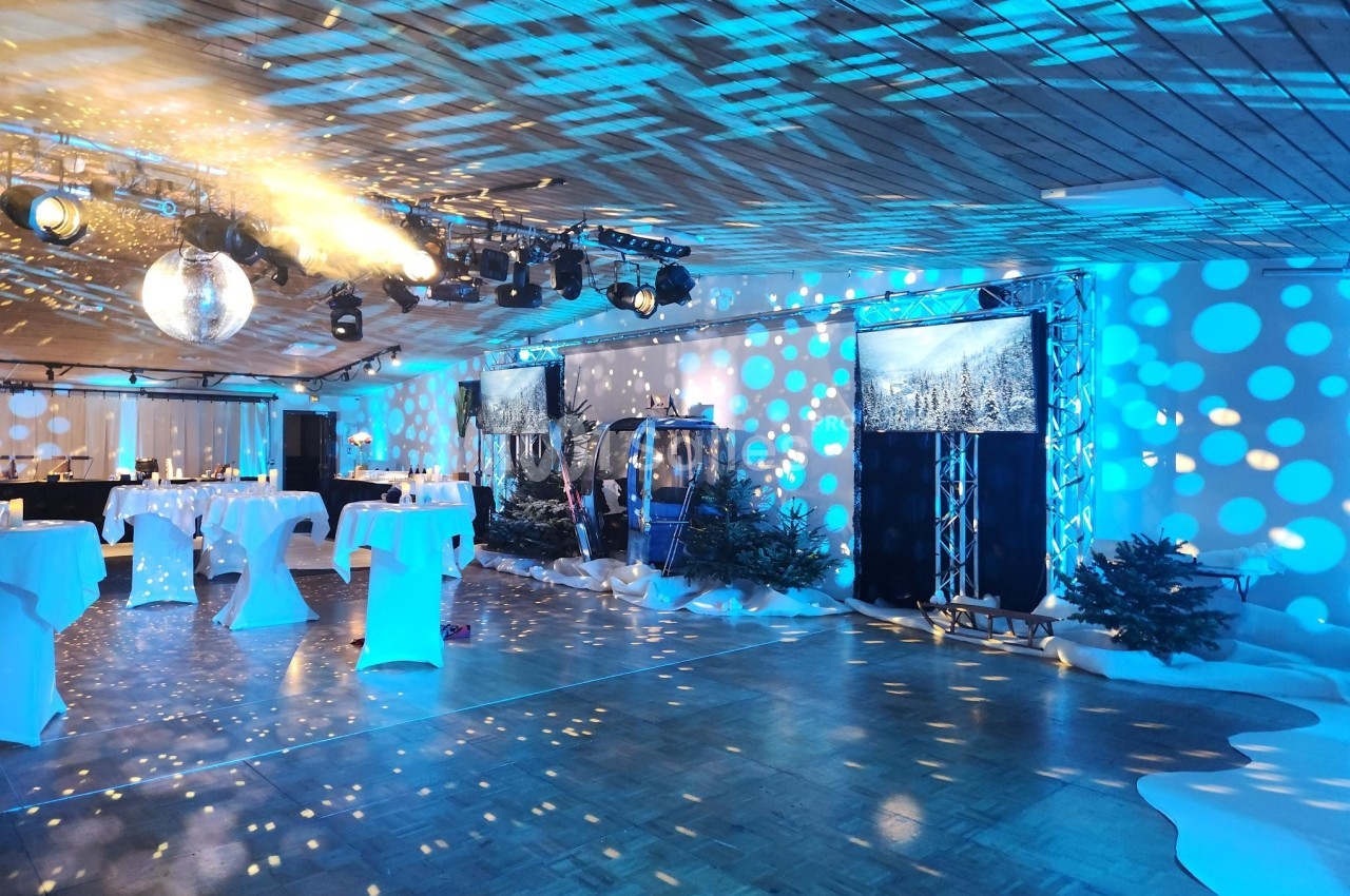 Salle décorée avec des lumières bleues, une boule disco, des tables hautes et des éléments évoquant un décor hivernal.
