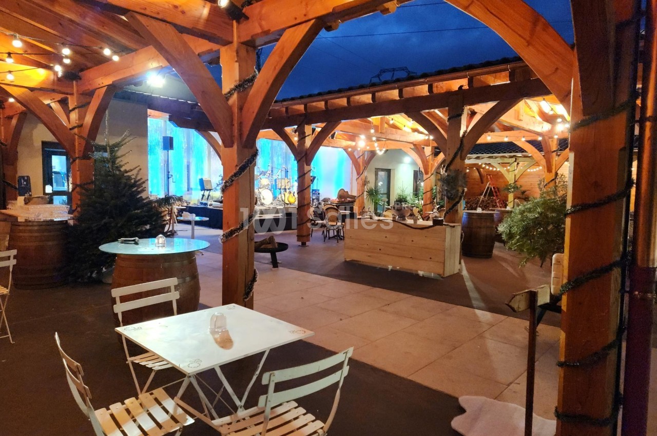 Terrasse couverte en bois avec tables blanches, guirlandes lumineuses et décorations, ambiance chaleureuse en soirée.