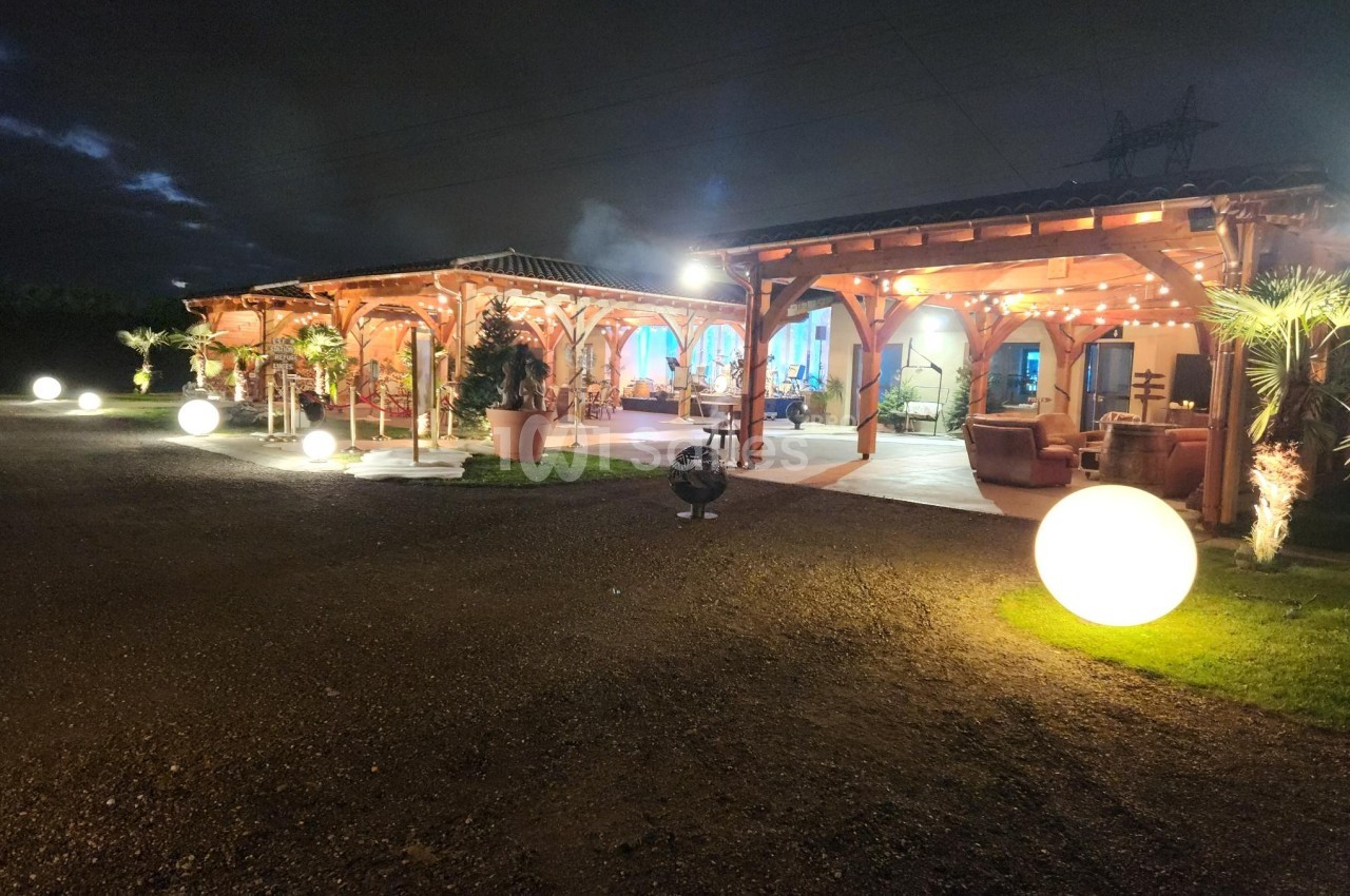 Terrasse éclairée d'un bâtiment en bois avec des lumières décoratives et des sphères lumineuses dans un cadre nocturne.