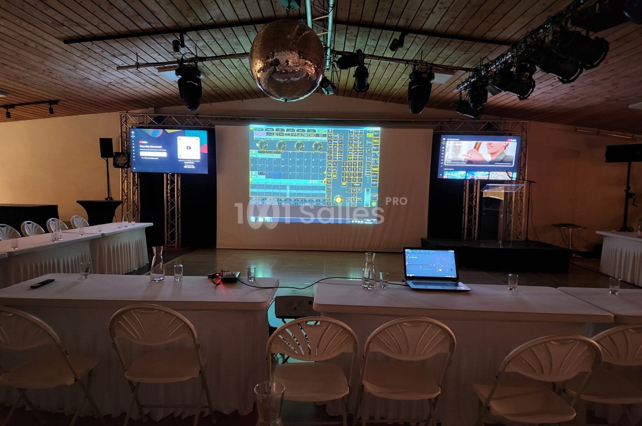 Salle de conférence équipée d'écrans, d'un projecteur affichant des graphiques et de tables disposées avec des chaises.