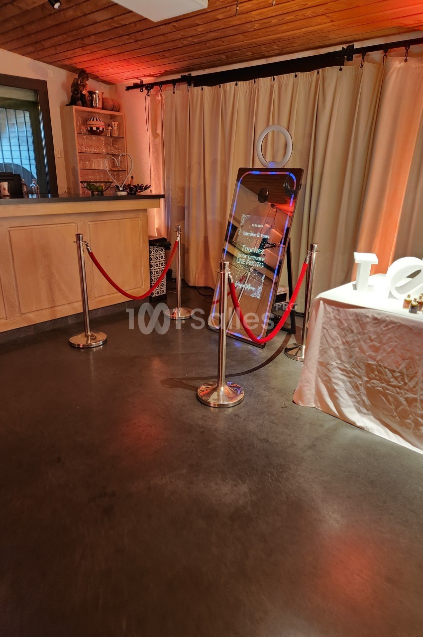Un miroir interactif entouré de cordons rouges dans une salle avec un comptoir et des rideaux beiges.