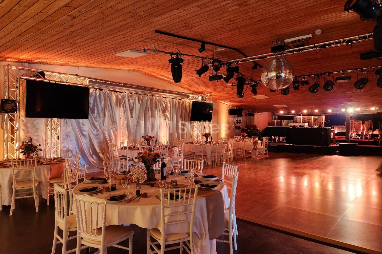 Salle de réception décorée avec des tables dressées, une piste de danse en bois et un éclairage chaleureux.