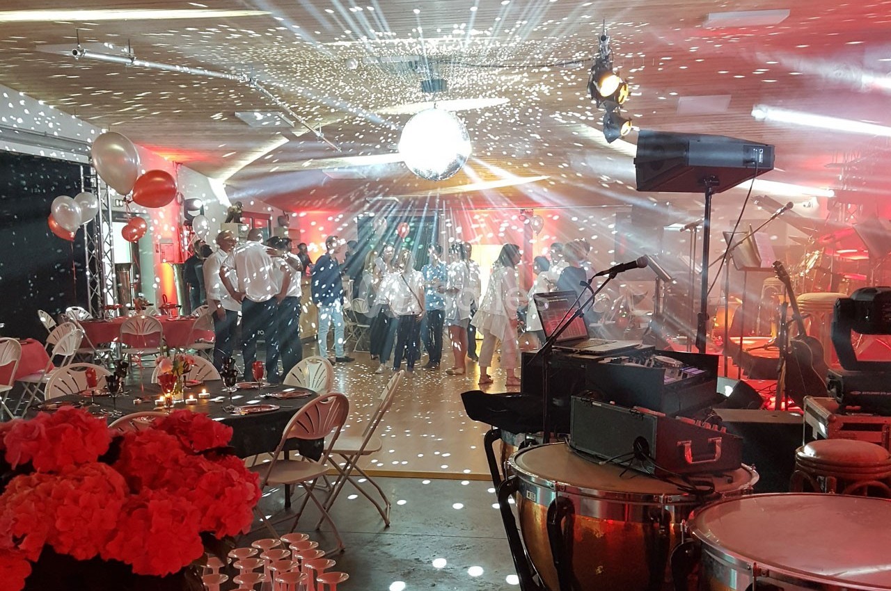 Salle décorée pour une fête avec une piste de danse éclairée par une boule à facettes et des invités en arrière-plan.