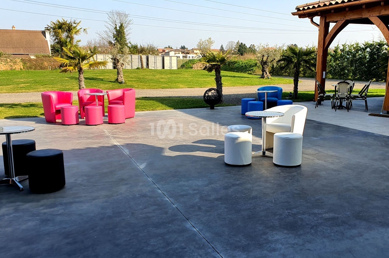 Terrasse avec mobilier coloré, tables et fauteuils, entourée de pelouse, palmiers et bâtiments en arrière-plan.