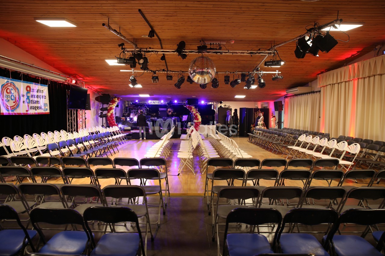 Salle aménagée avec des rangées de chaises face à une scène éclairée, prête pour un événement ou une performance.