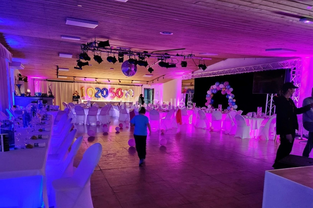 Salle de réception décorée avec des tables dressées, des ballons et des éclairages colorés, avec quelques personnes…