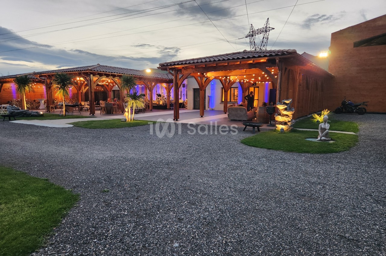 Terrasse éclairée en soirée avec des structures en bois, des plantes décoratives et un ciel partiellement nuageux.