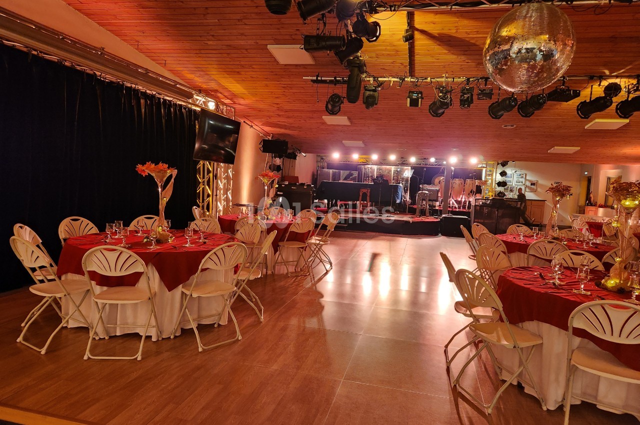 Salle de réception décorée avec des tables rondes, nappes rouges et blanches, éclairage chaleureux et piste de danse.