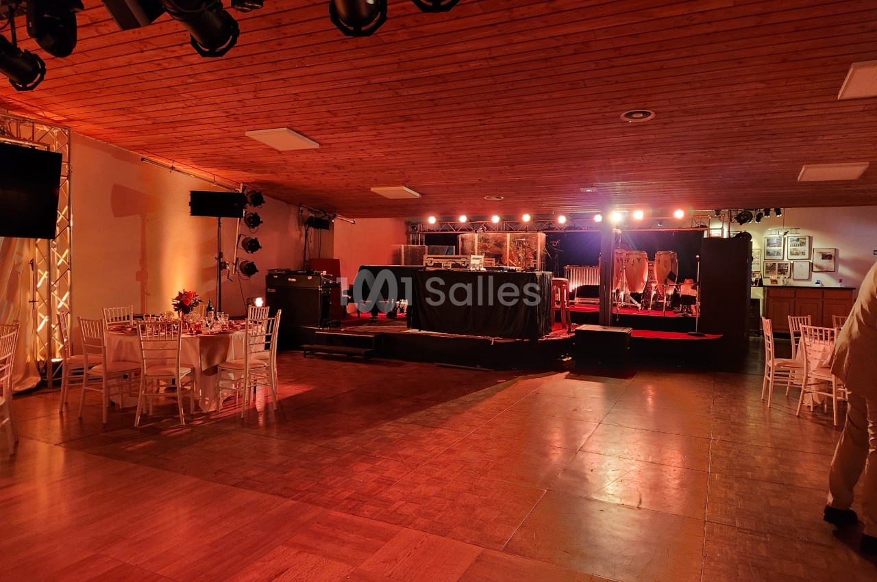Salle de réception avec piste de danse, tables dressées et scène éclairée équipée d'instruments de musique.