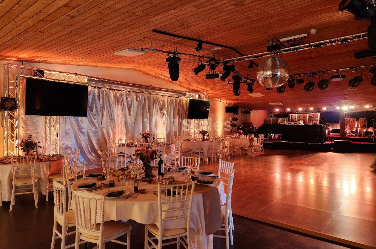 Salle de réception décorée avec des tables dressées, une piste de danse en bois et un éclairage chaleureux.